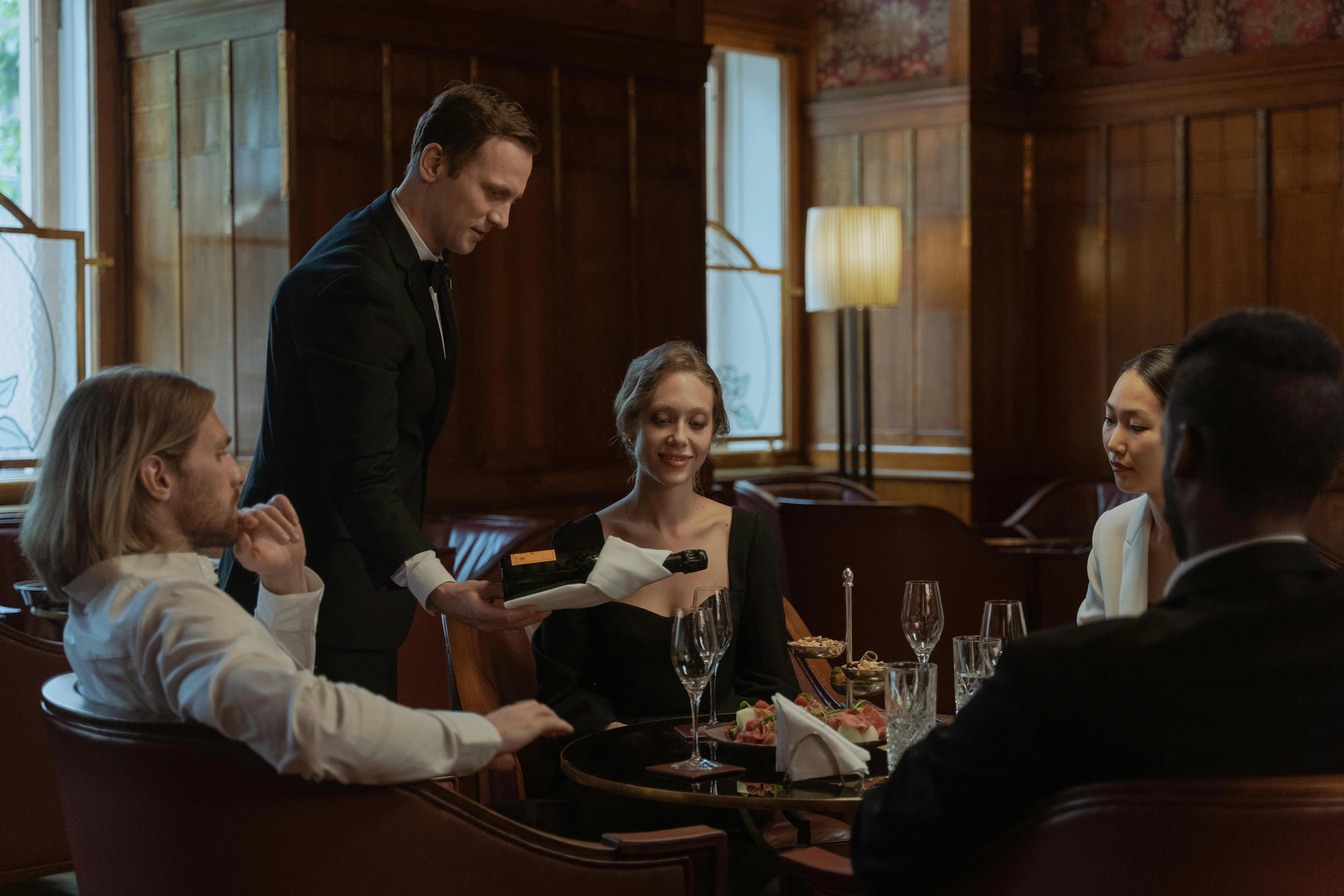 Restaurant server presenting a bottle at a dining table with seated guests