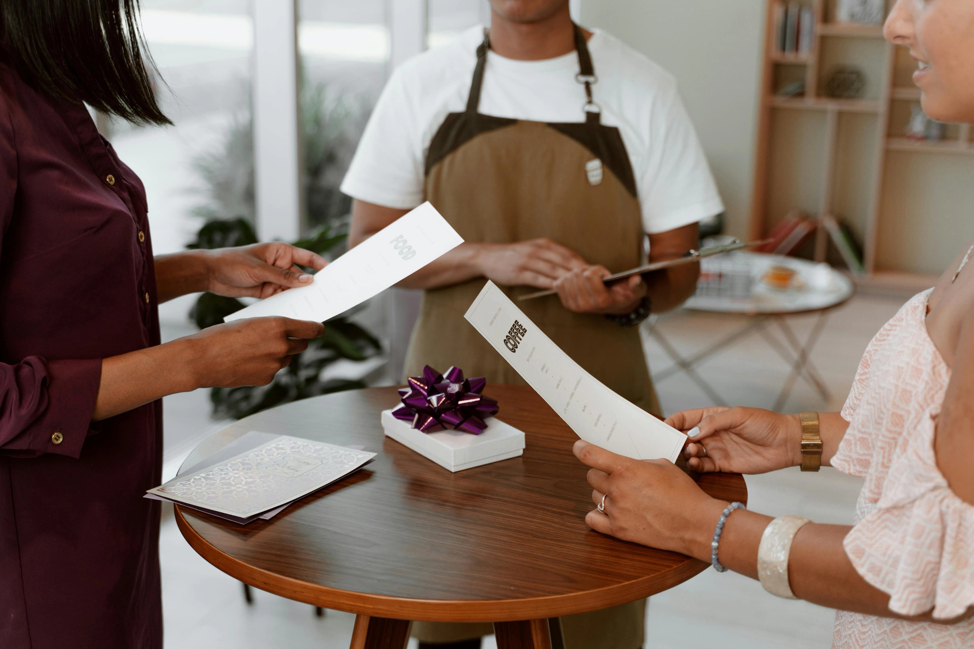 Server and guests reviewing menus at a restaurant table during active service